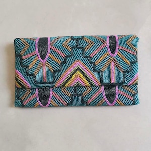 May include: A beaded clutch with a geometric pattern. The clutch features a teal background with pink, yellow, orange, and black beadwork. The flap is folded over, and the clutch is rectangular.