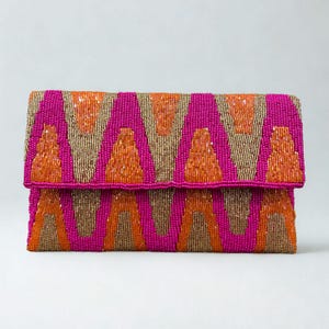 May include: A rectangular clutch with a fold-over flap, covered in small beads. The design features a repeating pattern of orange and gold triangles against a bright pink background. The clutch is a vibrant accessory.