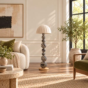 May include: A floor lamp featuring a stack of seven spherical, black and white marbled patterned beads as the central column, topped with a beige, pleated, dome-shaped lampshade and supported by a circular, light-toned wooden base.