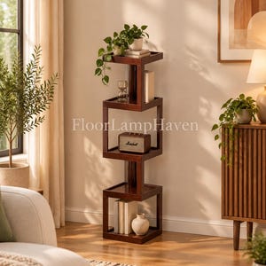May include: A tall, dark brown wooden shelving unit with a geometric, stacked square design. The unit features four open levels, each connected by a central vertical support, displaying a potted plant, a small speaker, and several books.