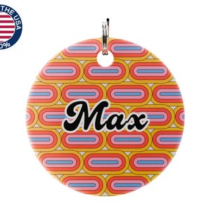 May include: A round pet tag with a retro design in yellow, orange, pink, and blue. The name "Max" is written in black script. The tag has a silver loop for attachment and a "Made in the USA" sticker.