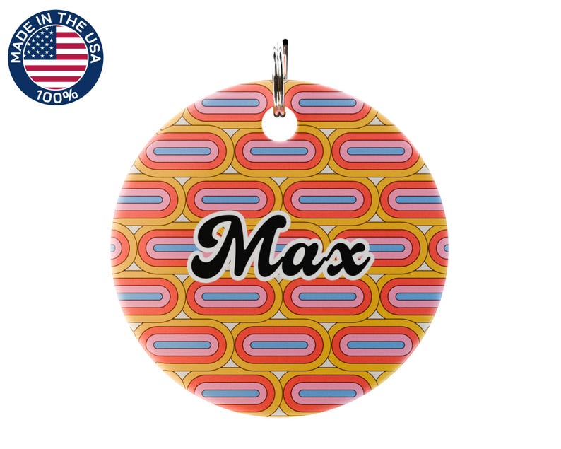 May include: A round pet tag with a retro design in yellow, orange, pink, and blue. The name "Max" is written in black script. The tag has a silver loop for attachment and a "Made in the USA" sticker.