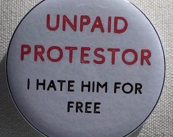 May include: A round button with a white background and black and red text. The text reads "UNPAID PROTESTOR I HATE HIM FOR FREE". The button has a black border.