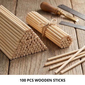 May include: A collection of 100 light-coloured wooden sticks arranged in a triangular stack and a cylindrical bundle tied with twine. A metal chisel and a metal ruler are visible nearby. The text 100 PCS WOODEN STICKS is printed at the bottom.