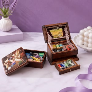 May include: Two dark brown wooden sewing boxes with lids and drawers. The open box contains colourful thread spools, needles, and lace trim. The lid of the closed box features a printed image of sewing supplies. Small gold scissors are visible inside.