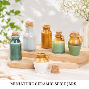 May include: A collection of six miniature ceramic spice jars with cork stoppers. The jars feature various glossy glazes in shades of green, blue, yellow, and white, with some designs including small handles. One jar is shown with its cork removed.