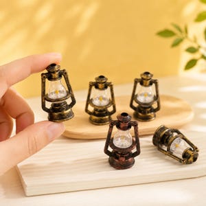 May include: A collection of miniature hurricane lanterns featuring a distressed bronze-colored metal finish, a clear glass globe, and a small internal light component. These small decorative lanterns are designed with a classic frame.