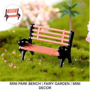 May include: Miniature park bench with a black frame and a reddish-orange seat. The bench is designed for a fairy garden or miniature decor. The bench is set on a bed of green moss.