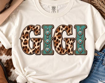 May include: An off-white short-sleeve t-shirt featuring the text GIGI printed across the chest. The letters G and G have a brown and black leopard print pattern, while the letters I and I are teal with silver concho accents.