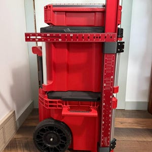 Könnte beinhalten: Eine rote Werkzeugkiste mit Rollen, schwarzem Griff und Rädern. Die Werkzeugkiste hat mehrere Fächer und ein eingebautes Lineal. Das Lineal ist etwa 35,5 cm lang. Die Werkzeugkiste ist für die Aufbewahrung von Werkzeugen konzipiert.