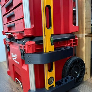 Könnte beinhalten: Roter Werkzeugkoffer mit Rollen, mehreren Schubladen und einer schwarzen und gelben Wasserwaage. Der Werkzeugkoffer trägt das Logo "Milwaukee PACKOUT". Die Truhe hat schwarze Räder und silberne Metallakzente.