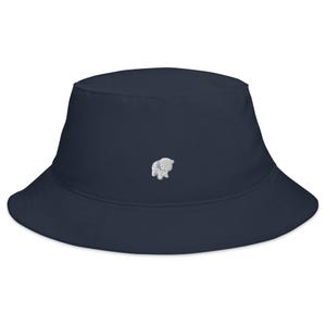 May include: A navy blue bucket hat featuring a white embroidered bear motif. The hat has a wide brim and a casual design. The bear is a small, embroidered detail on the front of the hat.