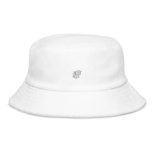 May include: A white bucket hat featuring a small, embroidered elephant motif. The hat has a wide brim and a soft, textured finish. This casual hat is suitable for sun protection and everyday wear.