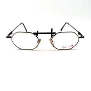 Puede incluir: Gafas vintage con montura de metal negro y lentes ovaladas. Las gafas presentan un diseño de puente único y la palabra "Casanova" está impresa en la lente derecha. El estilo general es retro y clásico.