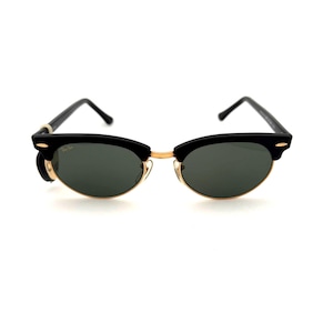 Peut inclure: Lunettes de soleil noires et dorées avec des verres vert foncé. Les lunettes ont un design classique à demi-monture avec une monture supérieure noire et une monture et des branches inférieures dorées. Les verres sont de forme ovale.