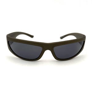 Puede incluir: Gafas de sol verde oliva oscuro con lentes gris oscuro. Las gafas tienen una montura gruesa y rectangular y patillas curvas. Las lentes son ligeramente curvadas y ofrecen cobertura total.