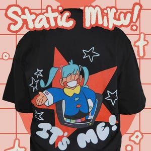 Könnte beinhalten: Schwarzes T-Shirt mit einer Cartoon-Figur mit blauen Haaren und einem blau-gelben Outfit, die aus einem roten Stern hervortritt. Das Shirt trägt die weißen Schriftzüge "Static Miku!", "It's me!" und "t-shirt".
