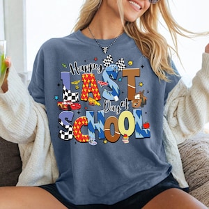 Peut inclure: Un t-shirt bleu avec l'inscription "Happy Last Day of School" dans des lettres color&eacute;es et ludiques. Le motif comprend des voitures de course, un drapeau &agrave; damier et une voiture de dessin anim&eacute;. Le t-shirt est port&eacute; par une personne portant des lunettes de soleil.