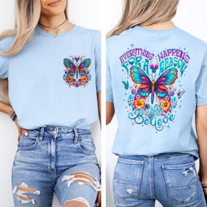 May include: Light blue t-shirt with a colorful butterfly design on the front and back. The front features a butterfly and floral design in a pocket. The back of the shirt has the text "Everything Happens For A Reason, Just Believe".