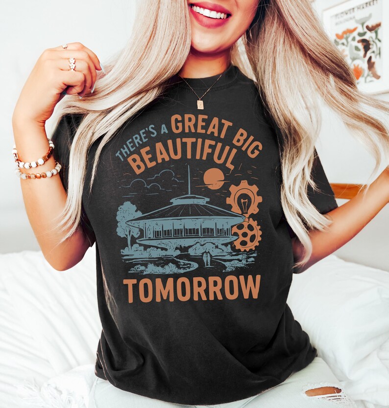 May include: Black t-shirt featuring a retro-style graphic with the text "There's a Great Big Beautiful Tomorrow." The design includes a futuristic building, a sun, and gears in shades of orange and blue. A vintage-inspired tee.