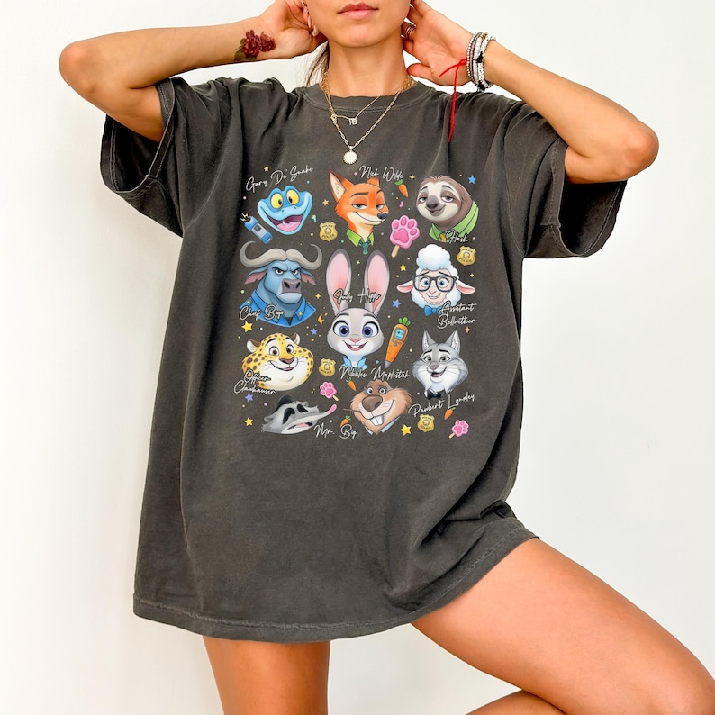 May include: A charcoal gray oversized t-shirt featuring a colorful graphic print of various animated animal characters from Zootopia, including Judy Hopps, Nick Wilde, Flash, and Chief Bogo, arranged with small icons like carrots and paw prints.