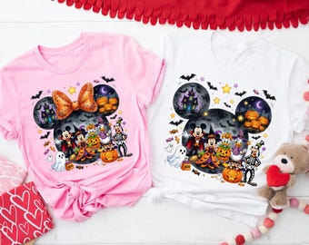 May include: A light pink t-shirt and a white t-shirt, each featuring a graphic of Mickey Mouse and friends in Halloween costumes. The design includes a large Mickey-shaped silhouette filled with a haunted house, pumpkins, bats, and stars.
