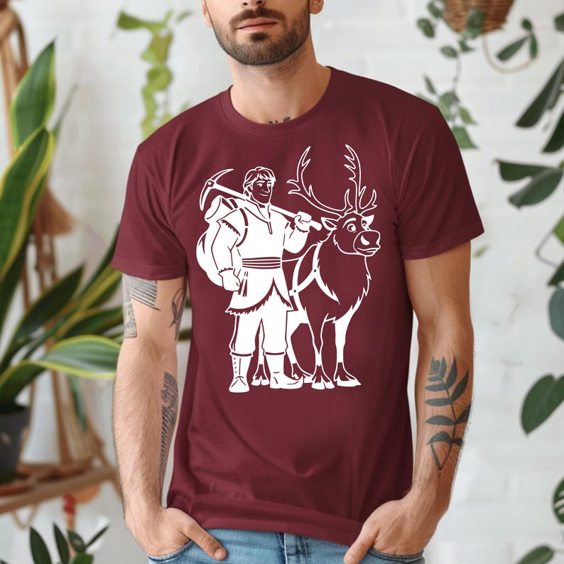 Op de afbeelding: Bordeauxrood t-shirt met een witte cartoon illustratie van een personage met een pikhouweel en een rendier. Het shirt met korte mouwen is gemaakt van zacht materiaal.
