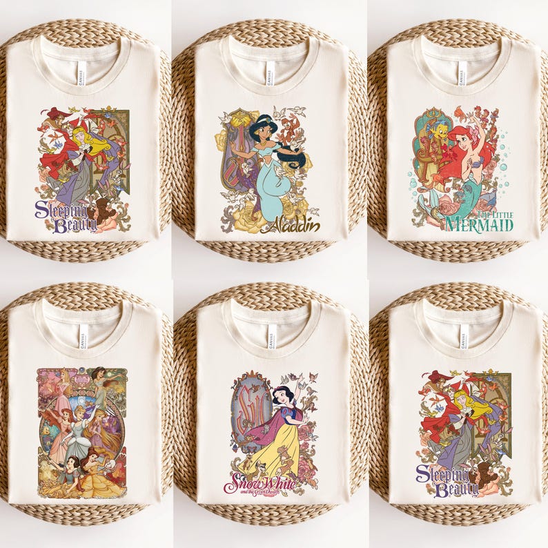 May include: A collection of six cream-colored t-shirts, each featuring a different graphic print of a classic animated character. The designs include Sleeping Beauty, Aladdin, The Little Mermaid, a group of princesses, and Snow White with floral motifs.