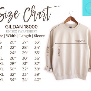 Op de afbeelding: Een beige Gildan 18000 unisex sweatshirt hangt aan een houten hanger. De afbeelding bevat een maattabel met afmetingen in inches, omgerekend naar cm. De tabel geeft breedte, lengte en mouwmaten voor de maten S t/m 5XL.