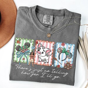 May include: A charcoal gray t-shirt featuring a graphic print of three rectangular panels with Moana, Pua the pig, and character-themed mouse ears. The text "There's just no telling how far I'll go" is printed in white script below the graphics.