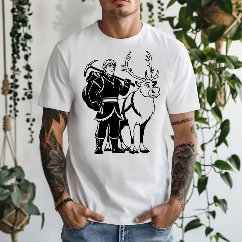 Op de afbeelding: Wit t-shirt met een zwart-witte afbeelding van een personage met een pikhouweel en een rendier. Het personage draagt een donkere outfit en draagt een tas. Het rendier heeft een harnas.