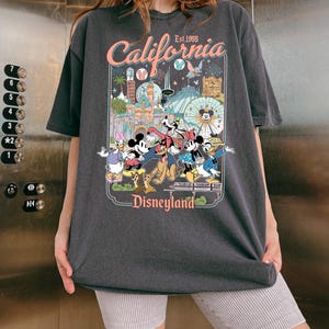 Op de afbeelding: Donkergrijs T-shirt met een Disneyland-afbeelding. De afbeelding bevat de tekst "California Est. 1955" en afbeeldingen van Mickey Mouse, Minnie Mouse, Donald Duck en andere Disney-personages. Het T-shirt heeft een losse pasvorm.