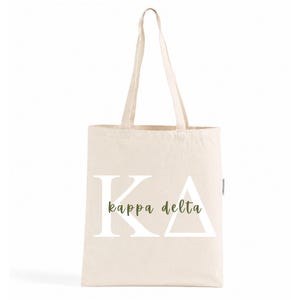 Könnte beinhalten: Eine naturfarbene Stofftasche aus Segeltuch mit den weißen griechischen Buchstaben Kappa Delta in großer Schrift, wobei die Wörter kappa delta in einer kleineren, olivgrünen Schreibschrift mittig über die Buchstaben gedruckt sind.