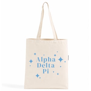 Peut inclure: Un sac fourre-tout en toile couleur crème avec le texte bleu Alpha Delta Pi imprimé au centre. Le motif est entouré d'icônes d'étoiles à quatre branches de différentes tailles dans la même couleur bleue, avec deux longues anses.
