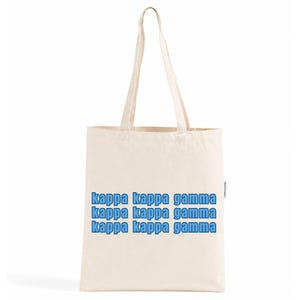 Könnte beinhalten: Eine cremefarbene Tragetasche aus Segeltuch mit zwei langen Schulterriemen. Auf der Vorderseite ist der Text "kappa kappa gamma" in drei horizontalen Zeilen in einer fetten, hellblauen Schrift mit dunkelblauem Rand aufgedruckt.