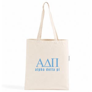 Könnte beinhalten: Eine naturfarbene Tragetasche aus Segeltuch mit zwei langen Schulterriemen. Auf der Vorderseite der Tasche befinden sich die griechischen Buchstaben ΑΔΠ in Hellblau, mit dem Text "alpha delta pi" in hellblauer Schrift unter den Symbolen.