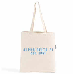 Op de afbeelding: Een natuurkleurige canvas draagtas met twee lange schouderbanden. De voorkant van de tas is voorzien van de tekst "ALPHA DELTA PI" in lichtblauwe hoofdletters, gevolgd door de tekst "est. 1851" in dezelfde lichtblauwe kleur en letterstijl.