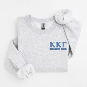 Puede incluir: Una sudadera gris claro con las letras griegas KKI en azul, con las palabras "kappa kappa gamma" debajo. Las mangas están dobladas. La etiqueta de la marca Gildan es visible.