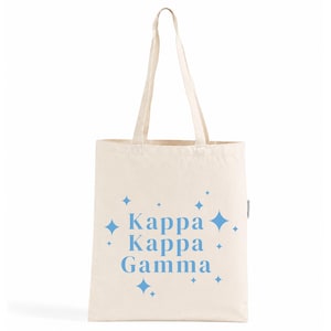 Peut inclure: Un sac fourre-tout en toile couleur crème avec deux longues bretelles. L'avant du sac présente le texte bleu clair "Kappa Kappa Gamma" centré, entouré de diverses tailles d'icônes d'étoiles à quatre branches bleu clair dispersées autour du texte.