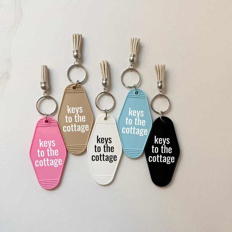 May include: Five motel-style keychains in pink, tan, white, light blue, and black. Each keychain has a silver ring and a tassel. The text "keys to the cottage" is printed on each keychain.