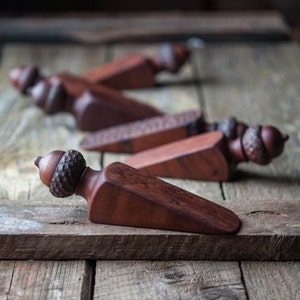 May include: A set of five wooden doorstops shaped like acorns. The doorstops are made of dark wood and have a natural finish. They are arranged in a row on a wooden surface.