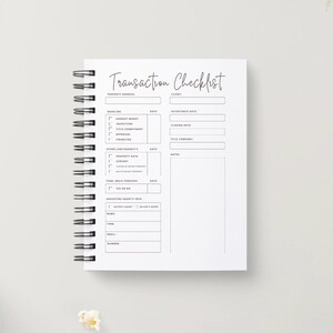 May include: A white spiral-bound notebook with the words "Transaction Checklist" in cursive script. The notebook has sections for property address, deadlines, and other details. A pencil and a bowl of popcorn are in the background.