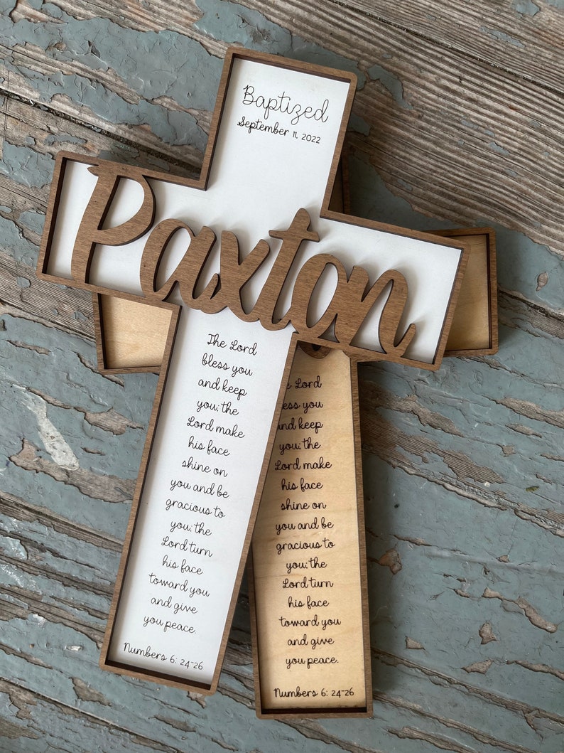 Peut inclure: Une croix en bois avec le nom "Paxton" grav&eacute; dessus. La croix est d&eacute;cor&eacute;e d'un fond blanc et du texte "Baptis&eacute; le 11 septembre 2022". La croix comprend &eacute;galement un verset de la Bible, Nombres 6&nbsp;:&nbsp;24-26, qui se lit comme suit&nbsp;: &laquo;&nbsp;Que le Seigneur te b&eacute;nisse et te garde&nbsp;; que le Seigneur fasse briller sa face sur toi et te fasse gr&acirc;ce&nbsp;; que le Seigneur tourne son visage vers toi et te donne la paix.&nbsp;&raquo;