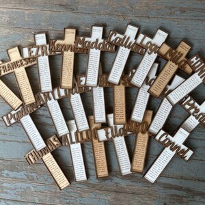 Peut inclure: Une collection de croix en bois avec des noms et un verset biblique imprim&eacute;s dessus. Les noms incluent Noah, Frances, Ezra, Kenny, Maddox, Callum, Log, Mila, Connor, Preston, Corbin, Thomas, Silas, Ella, Broc et Corvel.