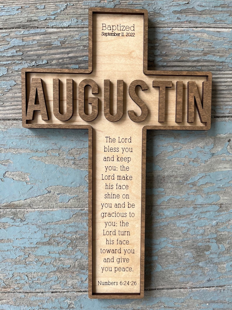 Peut inclure: Une croix en bois avec le nom "AUGUSTIN" grav&eacute; dessus. La croix est d&eacute;cor&eacute;e du texte "Baptized September 11, 2022" et d'un verset biblique : "L'&Eacute;ternel te b&eacute;nisse et te garde : l'&Eacute;ternel fasse briller sa face sur toi et te fasse gr&acirc;ce : l'&Eacute;ternel tourne sa face vers toi et te donne la paix. Nombres 6:24-26"