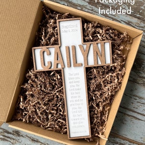 Peut inclure: Une croix en bois avec le nom "CAILYN" grav&eacute; dessus. La croix est dans une bo&icirc;te brune avec du papier d&eacute;chiquet&eacute;. La croix porte &eacute;galement le texte "Baptis&eacute; le 11 mai 2024" et un verset biblique : "L'&Eacute;ternel te b&eacute;nisse et te garde : l'&Eacute;ternel fasse briller sa face sur toi et te fasse gr&acirc;ce : l'&Eacute;ternel tourne sa face vers toi et te donne la paix, Nombres 6:24-26"