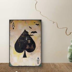 以下が含まれることがあります： 黒いスペードのエースのデザインが施された額入りのアートワーク。スペードの形は、城、人物、コウモリの暗いシーンで満たされ、黄褐色を背景にしています。「Frameit App / Tablet / Web」というテキストが下部に表示されています。
