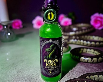 May include: A green glass bottle with a purple stopper and a chain, labelled "Viper's Kiss". The label features a green snake illustration. The bottle is filled with green liquid. The background includes a candle, pink roses, and snake-like decorations.