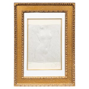 May include: A framed artwork featuring a white bas-relief sculpture of a nude figure. The artwork is set within a gold-colored, ornate frame. The sculpture depicts a woman with her arms raised. The artwork is signed.