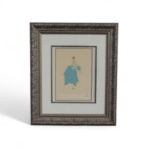 May include: Framed artwork featuring a figure in a blue and white striped dress. The artwork is set within a silver-toned, ornate frame. The artwork's background is a light beige color, and the figure is depicted with minimal detail.